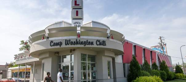 A white building with a rounded entry. Words above the door say Camp Washington Chili. A vertical sign is on top of the building made up of squares that spell CHILI.