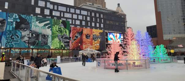 People skate around glowing trees with a large mural in the background.