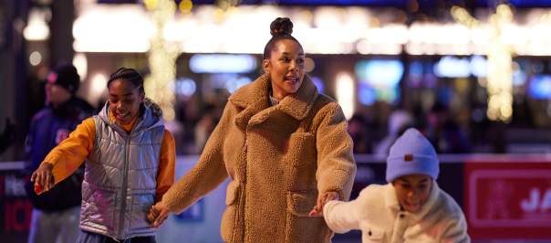 A mom and her two children ice skate while holding hands.