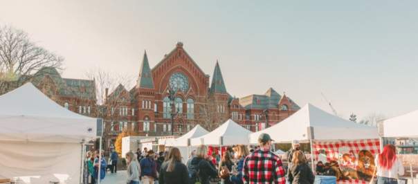 Image is of people shopping at vendor tents during the day in the winter with Cincinnati Music Hall in the background.