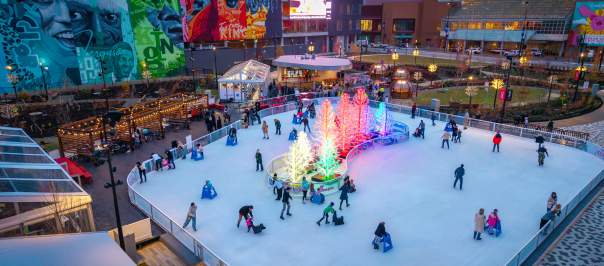 People skate on the ice rink around a cluster of glowing trees.