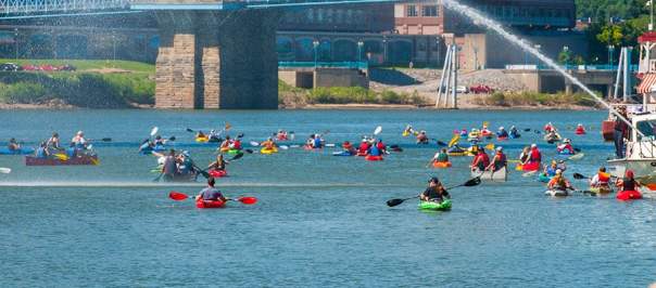 A large group of kayaks paddle under the Roebling Suspension Bridge in Covington, Kentucky during Paddlefest.