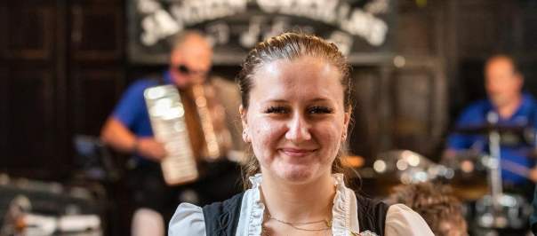 A smiling server walks towards the camera carrying two large beer steins in one hand.