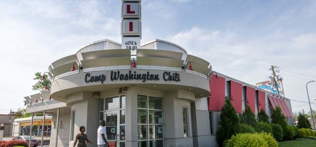 A white building with a rounded entry. Words above the door say Camp Washington Chili. A vertical sign is on top of the building made up of squares that spell CHILI.