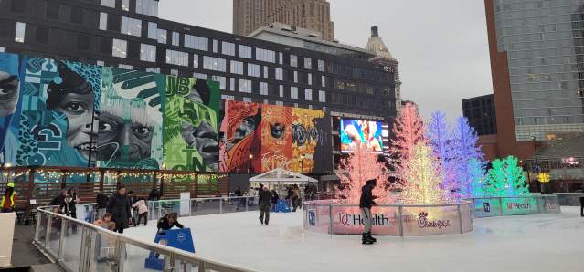 People skate around glowing trees with a large mural in the background.