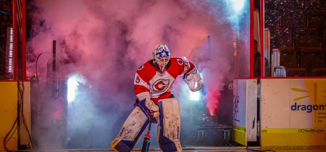 Image is of a hockey goalie entering the ice with smoke and lights to his back.