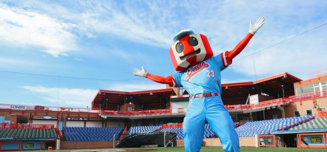 A red and white striped water tower mascot in a blue uniform stretches its arms wide with stadium seating behind.
