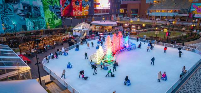 People skate on the ice rink around a cluster of glowing trees.