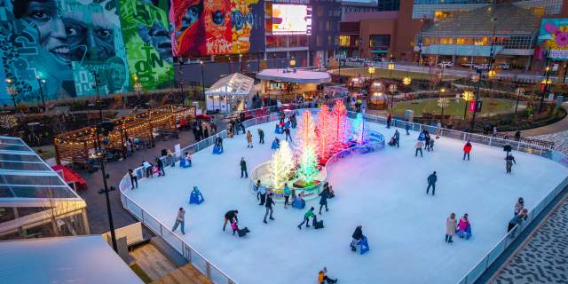 People skate on the ice rink around a cluster of glowing trees.