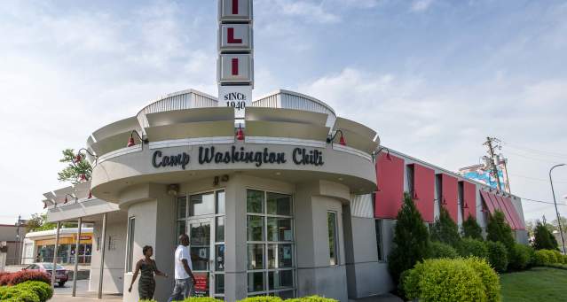 A white building with a rounded entry. Words above the door say Camp Washington Chili. A vertical sign is on top of the building made up of squares that spell CHILI.