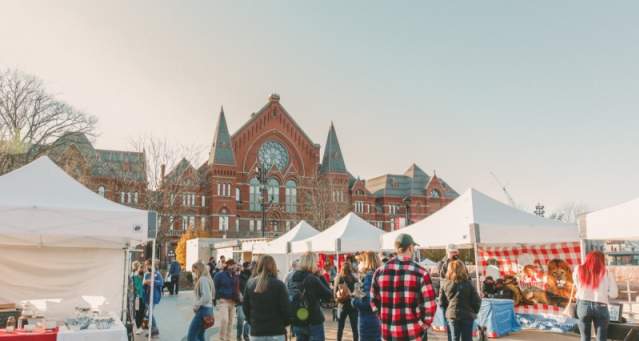 Image is of people shopping at vendor tents during the day in the winter with Cincinnati Music Hall in the background.