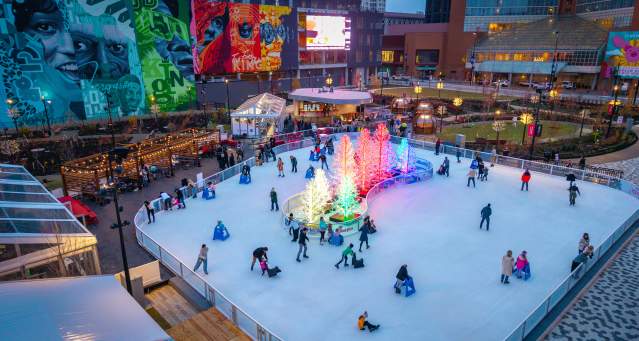 People skate on the ice rink around a cluster of glowing trees.