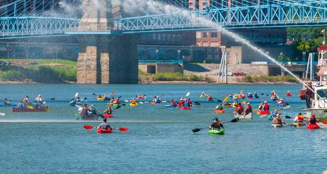 A large group of kayaks paddle under the Roebling Suspension Bridge in Covington, Kentucky during Paddlefest.