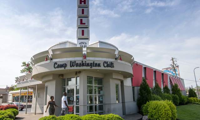 A white building with a rounded entry. Words above the door say Camp Washington Chili. A vertical sign is on top of the building made up of squares that spell CHILI.