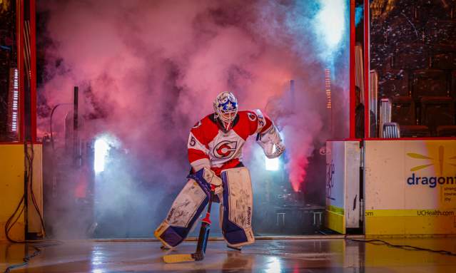 Image is of a hockey goalie entering the ice with smoke and lights to his back.