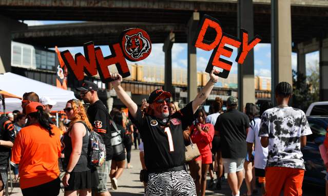 A group of tailgaters celebrate before a Bengals game - one fan, with his face painted, holds up a "Who Dey" sign.