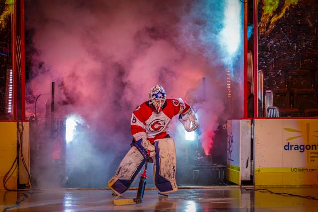 Image is of a hockey goalie entering the ice with smoke and lights to his back.