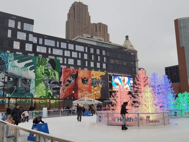 People skate around glowing trees with a large mural in the background.