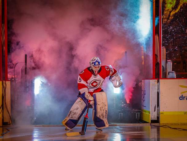 Image is of a hockey goalie entering the ice with smoke and lights to his back.