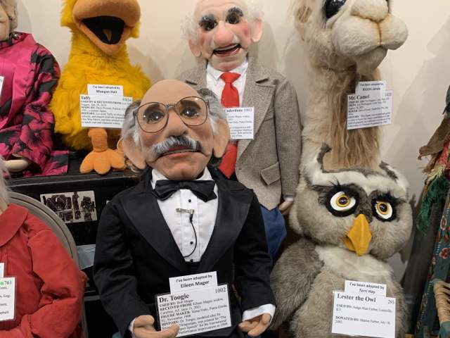 Several ventriloquism dummies posed with description cards.
