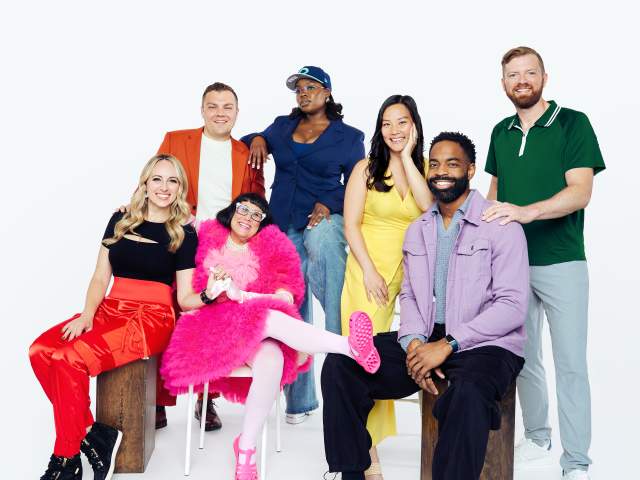 A group of 7 colorfully dressed individuals pose in front of the camera.