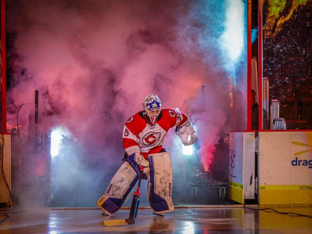 Image is of a hockey goalie entering the ice with smoke and lights to his back.