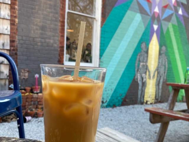 An iced coffee sit on a table in front of a vibrant mural.