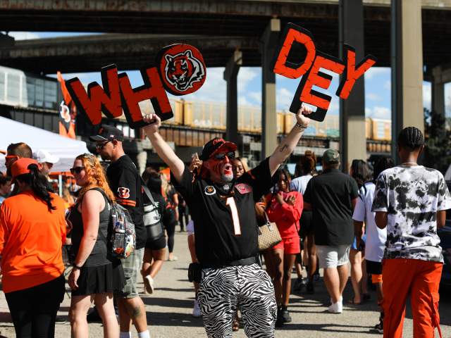 A group of tailgaters celebrate before a Bengals game - one fan, with his face painted, holds up a "Who Dey" sign.