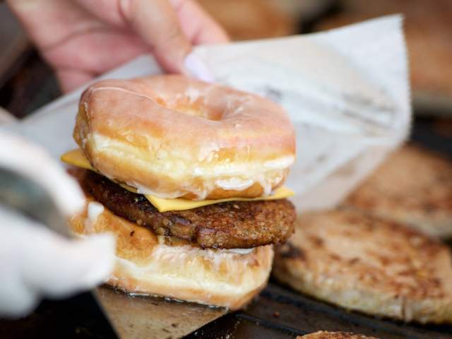 A hand picking up a sandwich made with a glazed donut, goetta, and cheese