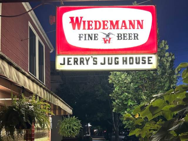 The exterior sign outside of Jerry's Jug House, lit up at night time.