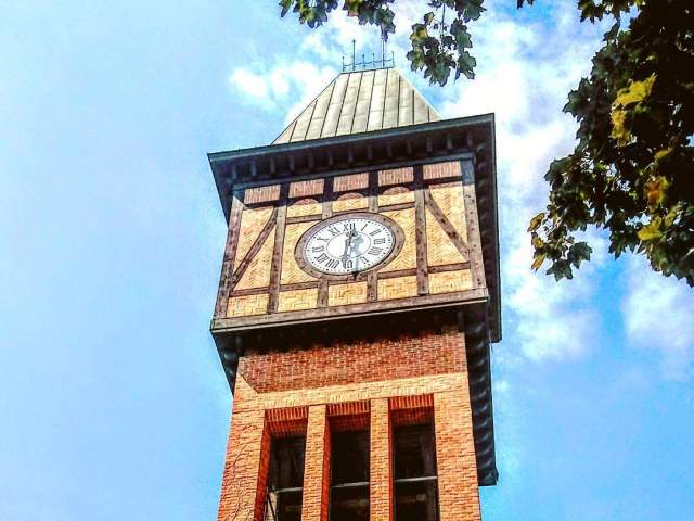 A brick, Bavarian clock tower ascends into the blue sky.