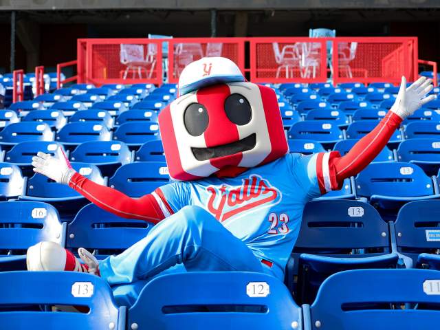 An anthropomorphic version of the famous red and white striped Florence, KY watertower, dressed in a blue and red Florence Y'alls uniform. It sits in the stadium seats arms stretched wide.