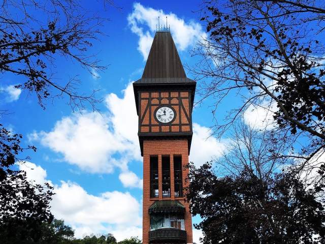 A brick clocktower with a glockenspiel against a blue sky with white clouds