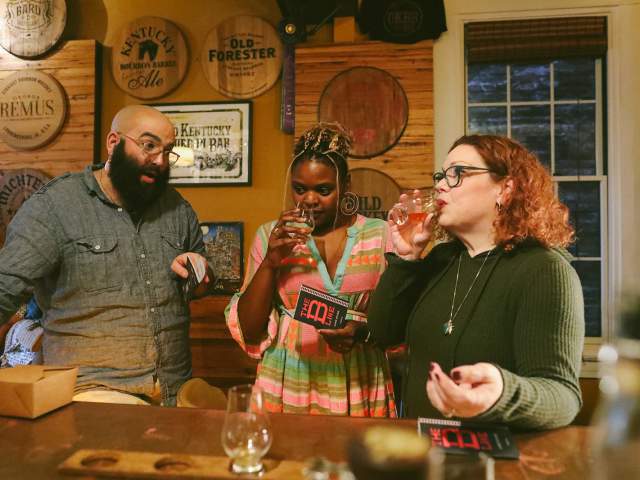 Three people at the bar at Old Kentucky Bourbon Bar. A man chats while two women sniff and sip bourbon.