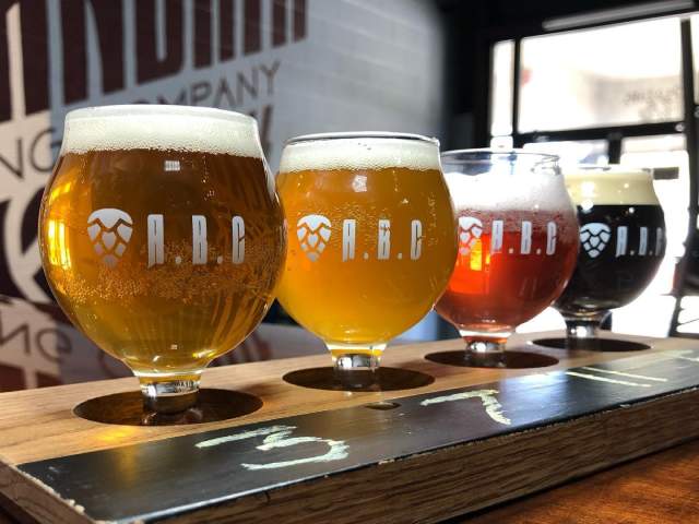 Four glasses of beer in a flight set in a wooden holder at Alexandria Brewing Company