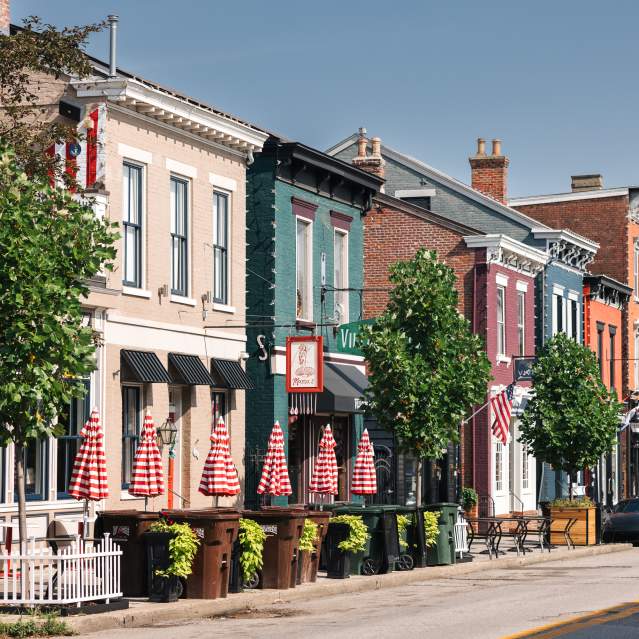 A line of buildings in various colors. There's trees and a grouping of red and white striped umbrellas.