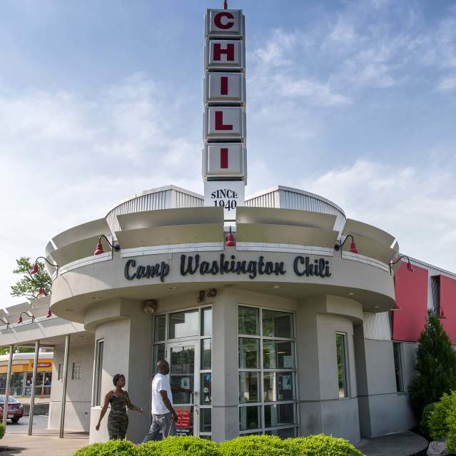 A white building with a rounded entry. Words above the door say Camp Washington Chili. A vertical sign is on top of the building made up of squares that spell CHILI.