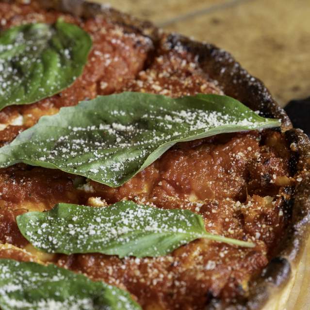 A deep dish, Chicago style pizza with fresh basil on top.