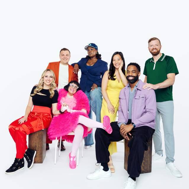 A group of 7 colorfully dressed individuals pose in front of the camera.