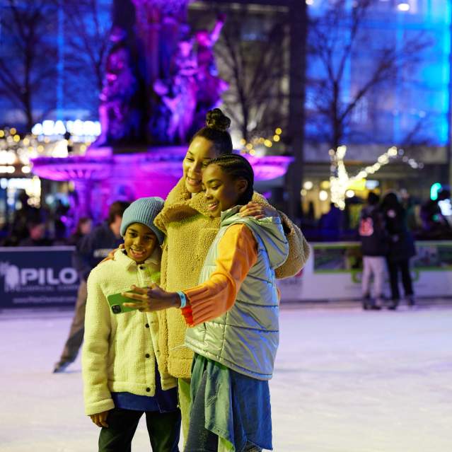 A family takes a selfie together while ice skating.