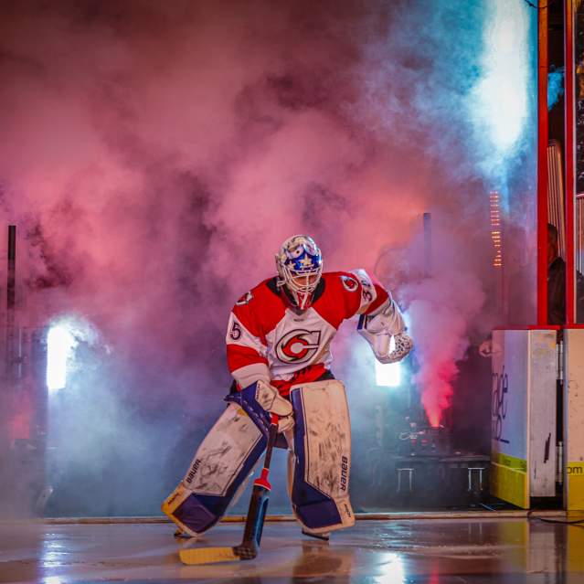 Image is of a hockey goalie entering the ice with smoke and lights to his back.
