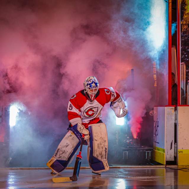Image is of a hockey goalie entering the ice with smoke and lights to his back.