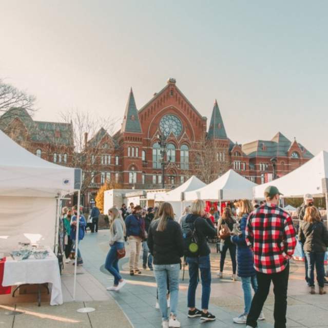 Image is of people shopping at vendor tents during the day in the winter with Cincinnati Music Hall in the background.