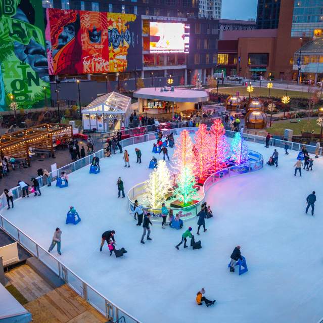 People skate on the ice rink around a cluster of glowing trees.