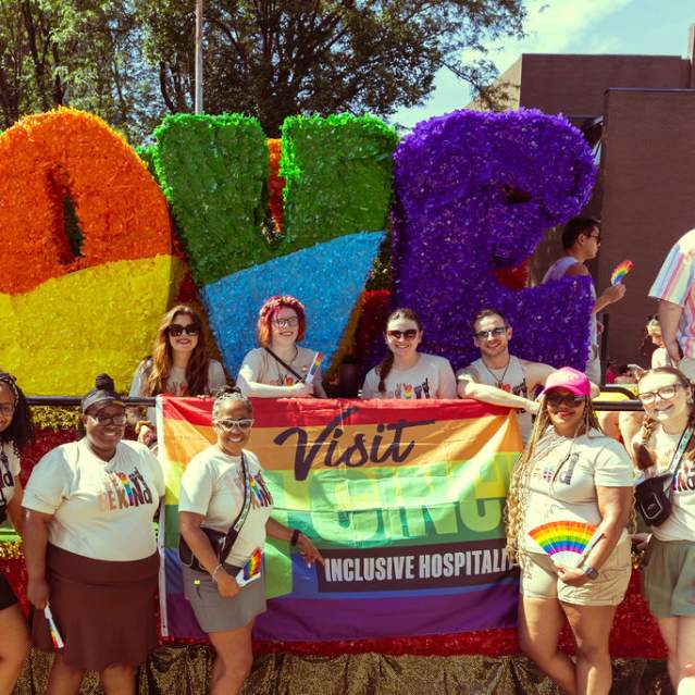 A group of Visit Cincy employees poses in front of a float for the Cincinnati Pride parade
