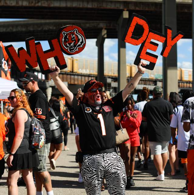 A group of tailgaters celebrate before a Bengals game - one fan, with his face painted, holds up a "Who Dey" sign.