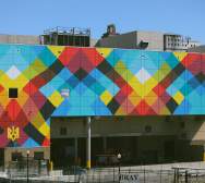 A large-scale mural on the side of a convention center features colorful criss-crossing line reminiscent of a weaving