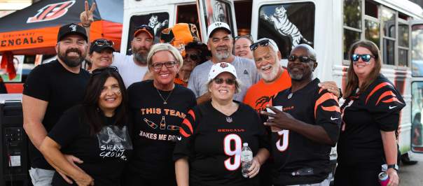 A group of 12 Bengals fans decked out in gear pose in front of a Bengals bus.