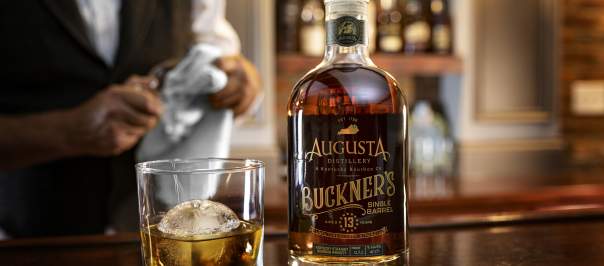 Image is of a bottle of Augusta Distillery's Buckner's Single Barrell and a glass of bourbon next to it with an ice ball.
