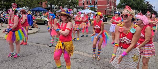 A group of people in red tops and brightly colored accessories dance at NKY Pride